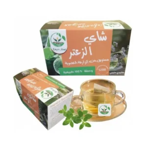 Deux boîtes de Tisane Azzaatar de ZaynJbel posées sur une table en bois devant un paysage de montagnes brumeuses, accompagnées d’une tasse transparente remplie d’infusion dorée — produit 100 % naturel, inspiré des traditions du Rif marocain.